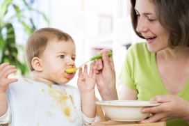 Joyous mother feeding cute messy baby boy with vegetable puree.